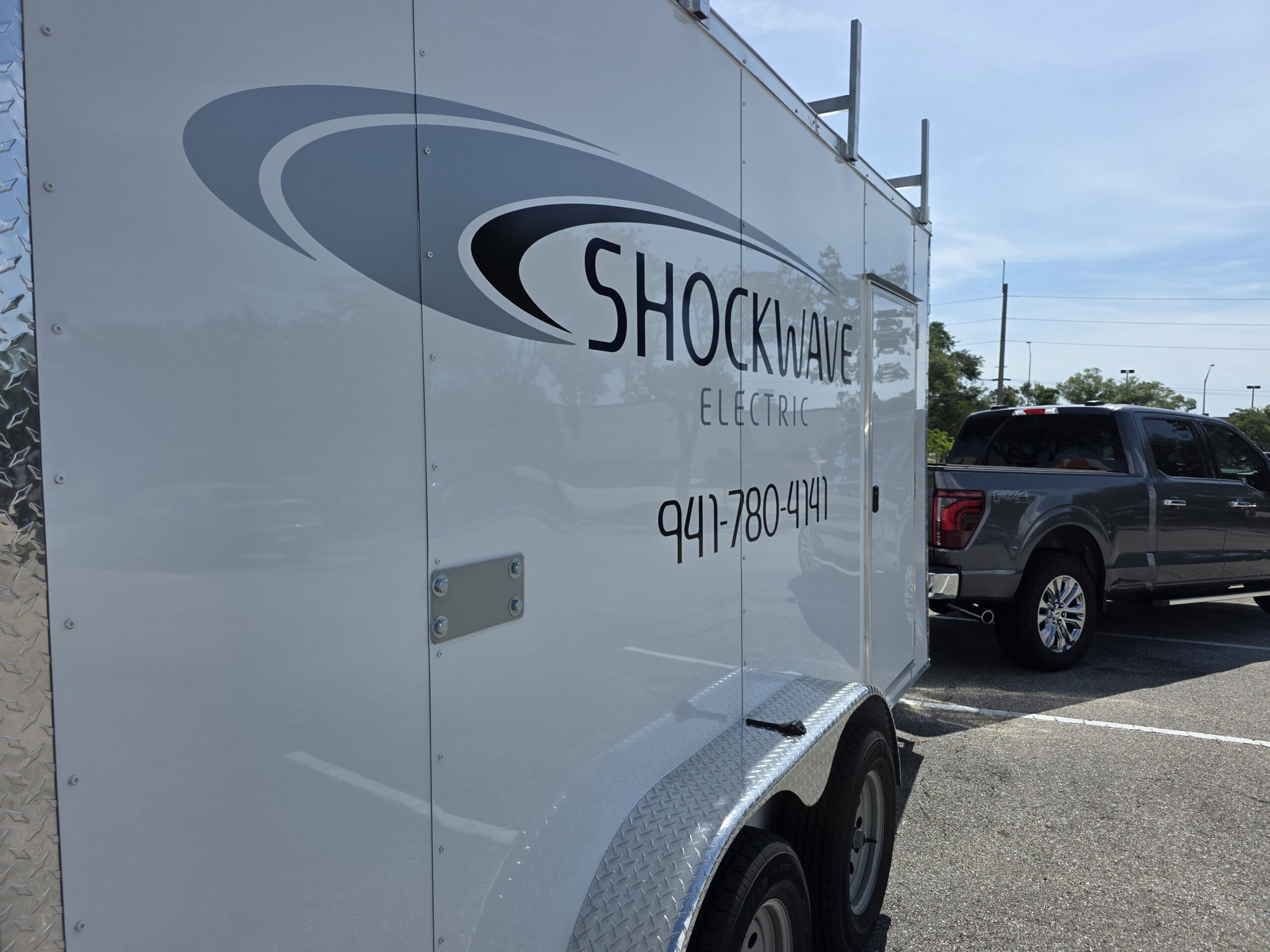 Shockwave Electric signwritten service trailer and pickup truck parked on a job